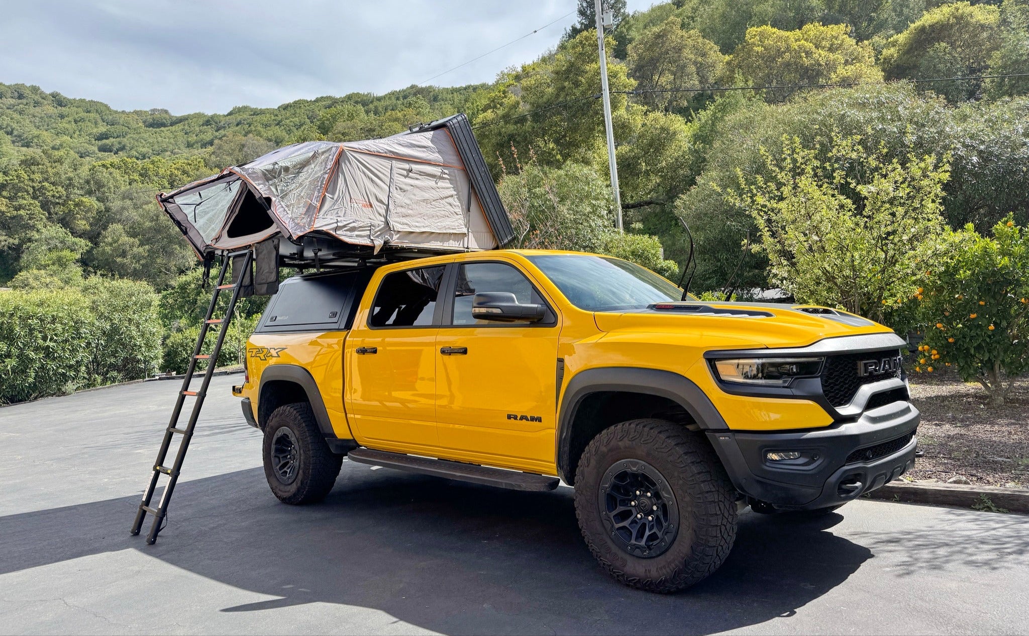 Yellow truck with a rooftop tent on a road surrounded by trees